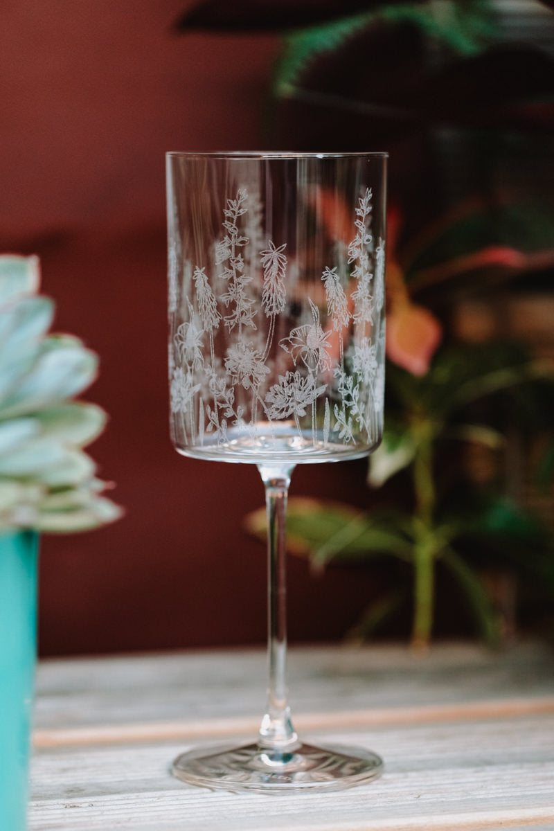 Etched glass goblet on a wooden surface with plants in the background