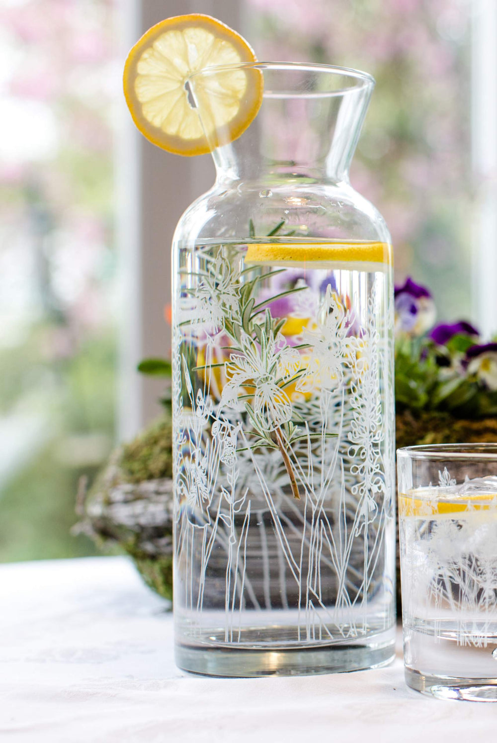 Decorative glass carafe with flowers and lemon slices on a table outdoors.
