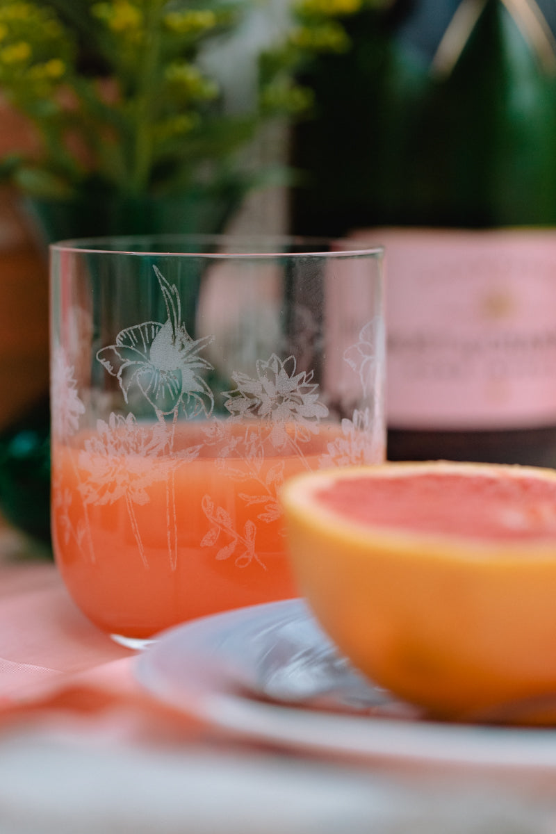 Glass of grapefruit Juice with a floral design next to a half-sliced grapefruit on a blurred background