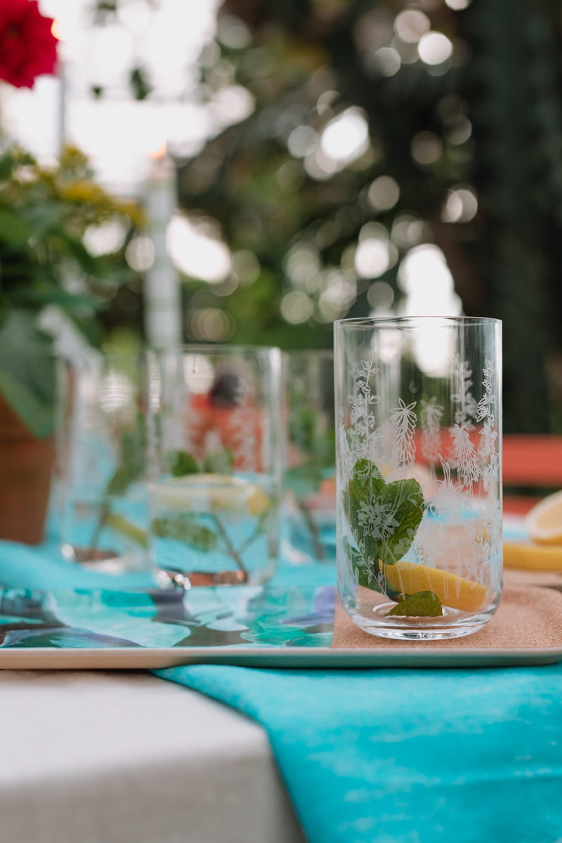 Clear glass with a leaf design on a table with a blue runner and blurred outdoor background