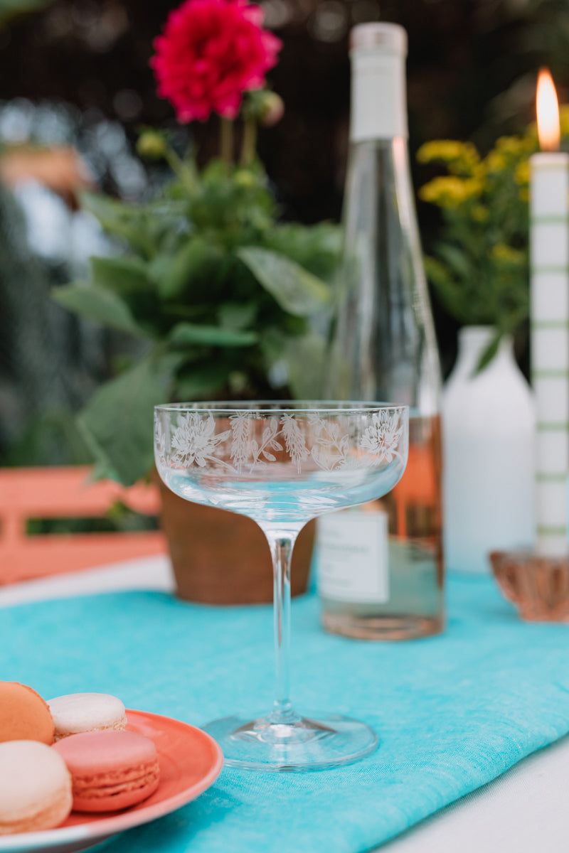 Cocktail glass with a blue drink on a table with flowers and candles in the background