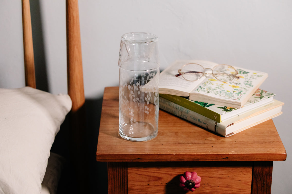 Clear glass vase on a wooden nightstand with books and glasses