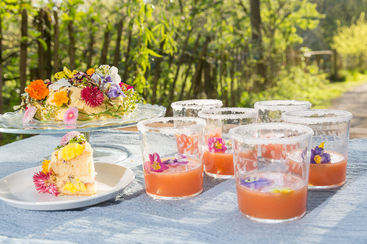 Outdoor setting with floral cakes and colorful drinks on a table.