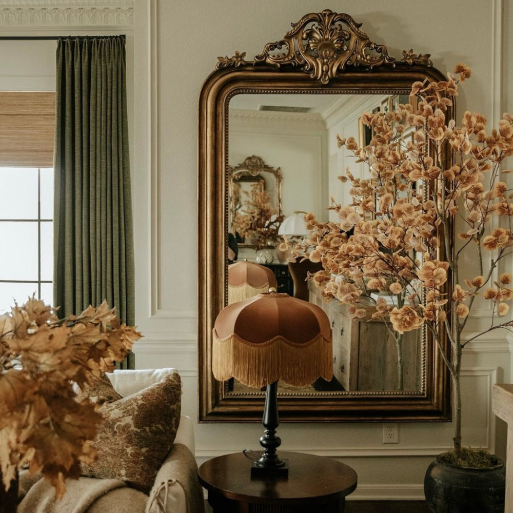 Decorative interior with ornate mirror, floral arrangements, and a lamp.