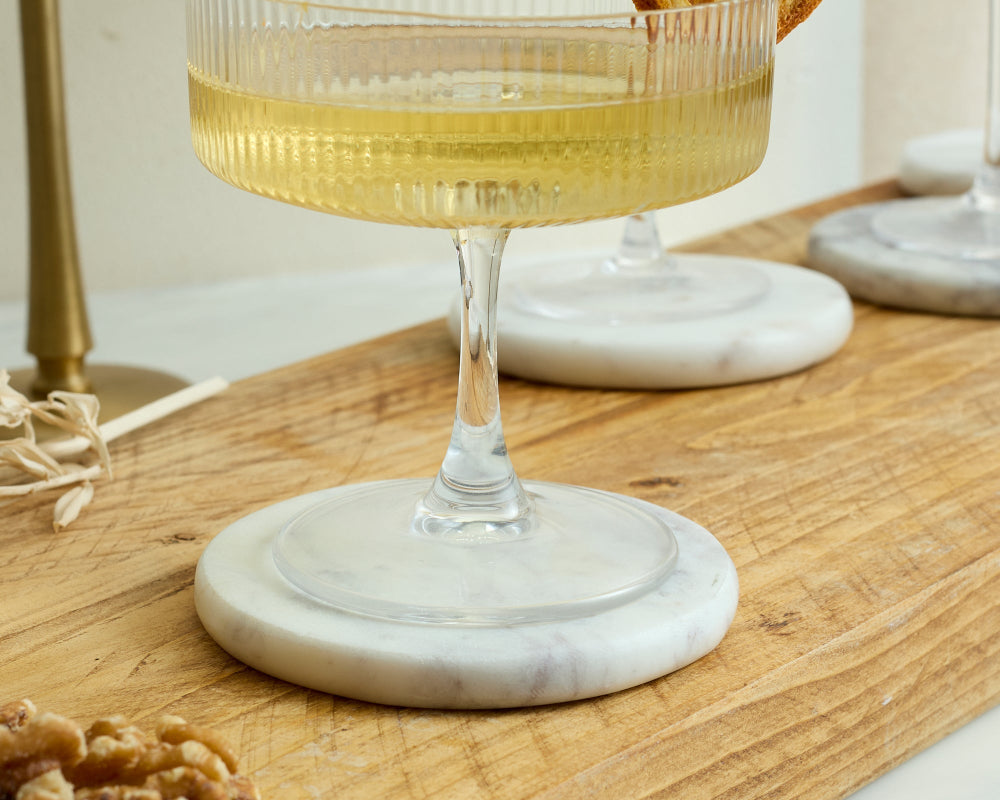Cocktail glass with a sparkling wine on a white and grey marble coaster on a wooden surface