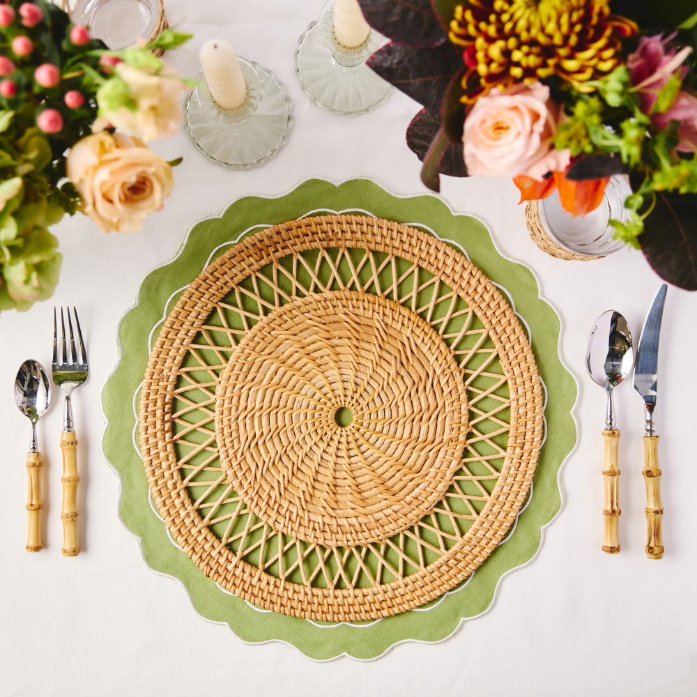 Rattan placemat on a white table with floral arrangements and cutlery.