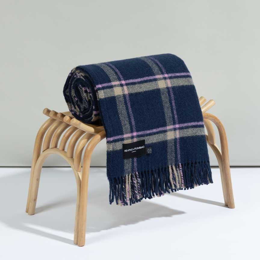 Navy plaid blanket with pink accents draped over a wooden stool on a light grey background