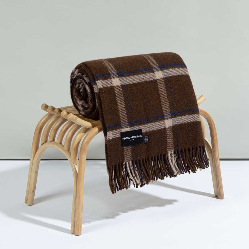 Brown plaid blanket on a wooden stool against a light grey background