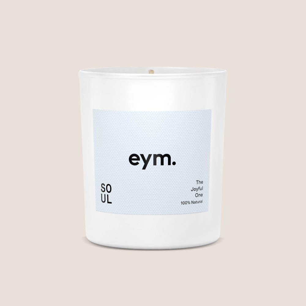 White candle with a blue label featuring the brand 'eym' on a beige background