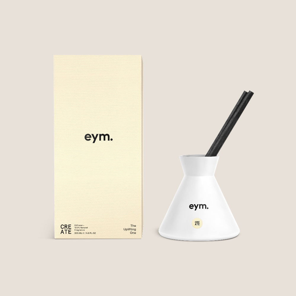 White Diffuser vessel with black reeds and yellow packaging featuring 'eym.' brand on a beige background