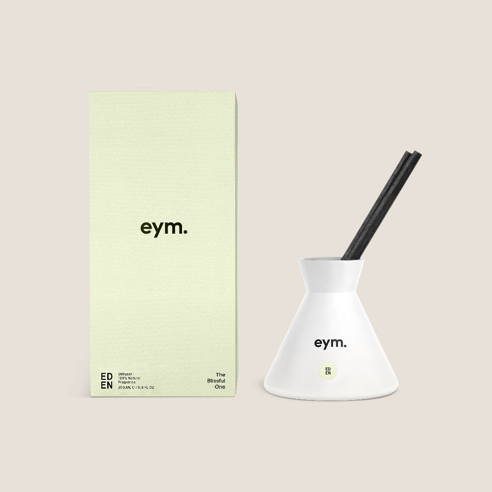 White home diffuser eym product with black reeds on a beige background with green packaging.