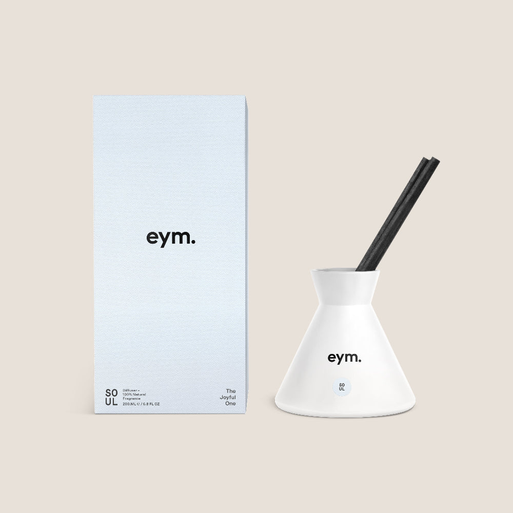 White Diffuser vessel with black reeds and 'eym.' branding next to a light blue box on a beige background