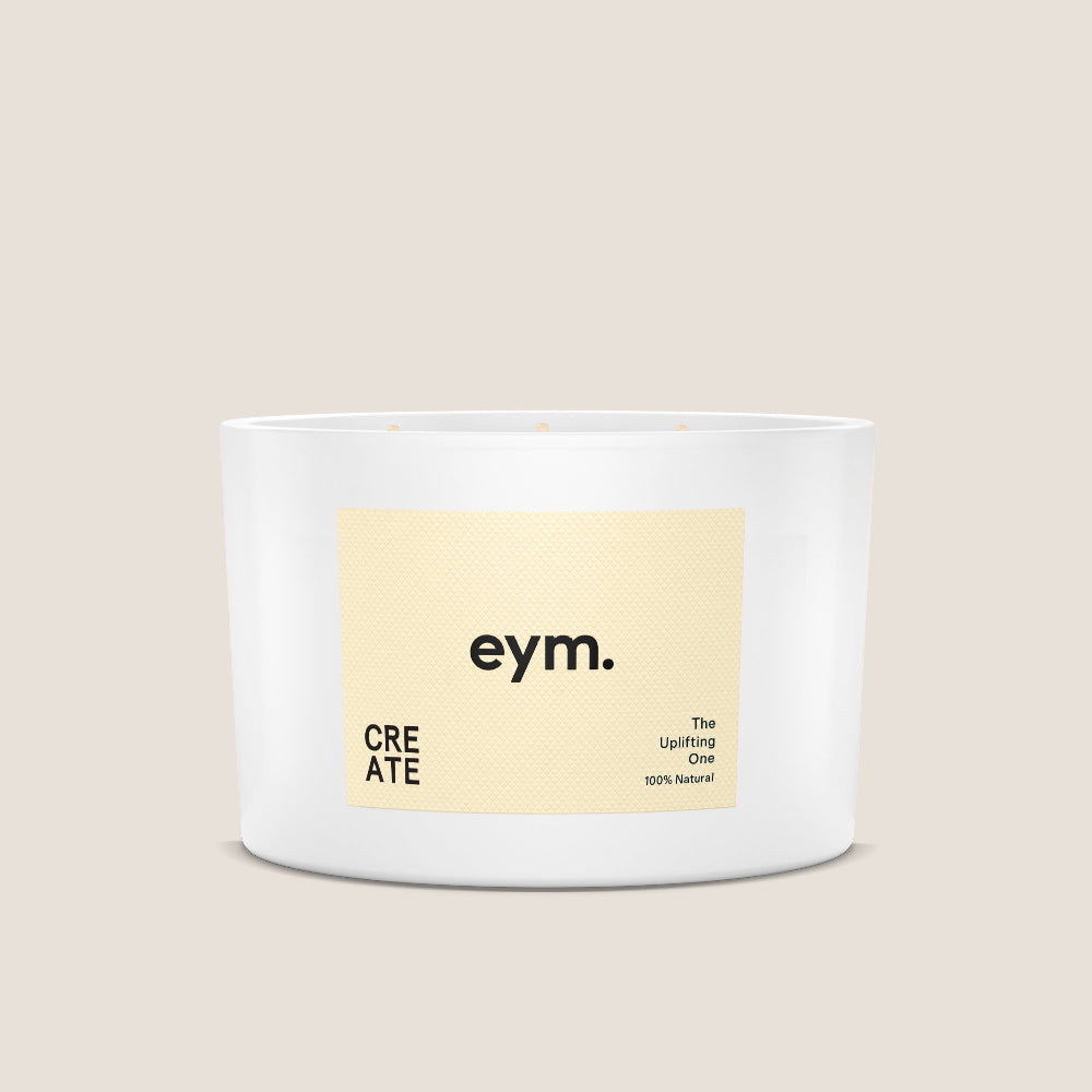 White candle with a beige label featuring the brand 'eym.' on a beige background