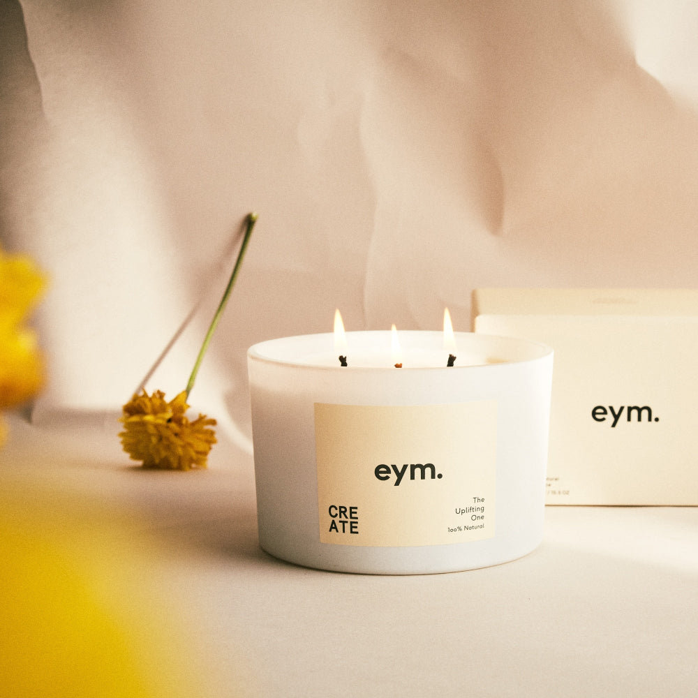 White candle with 'eym.' label on a soft background