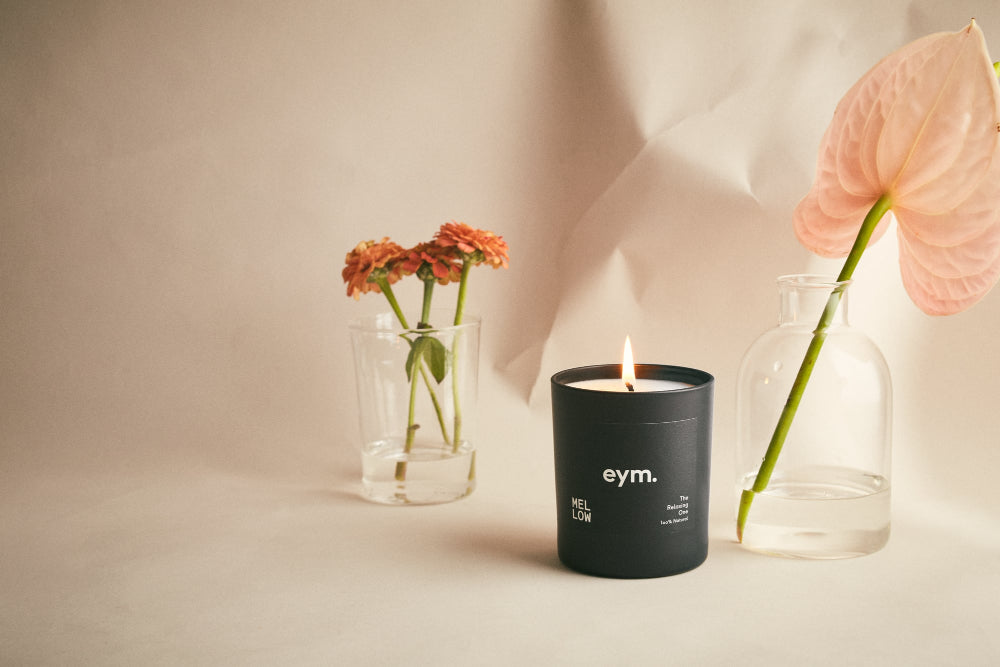 Black Candle vessel with 'eym' branding next to flowers in glass vases on a neutral background