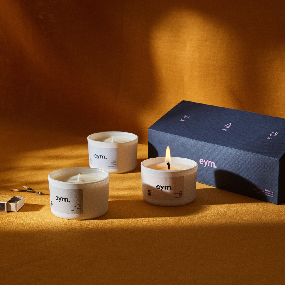 Three eym candles on a wooden surface with a dark blue box in the background.