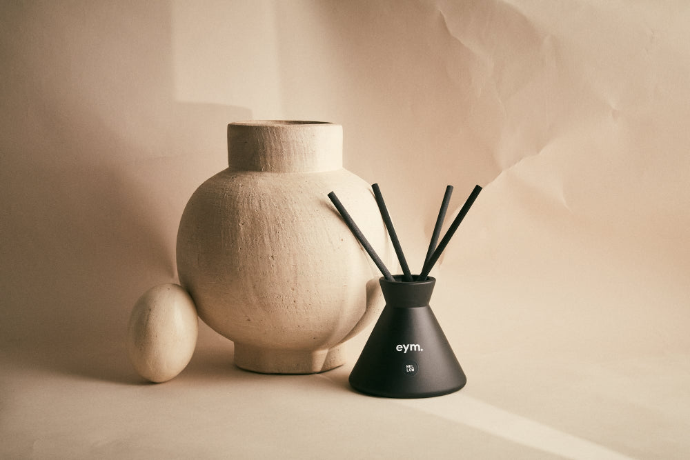 Black diffuser with sticks next to a beige ceramic vase on a beige background