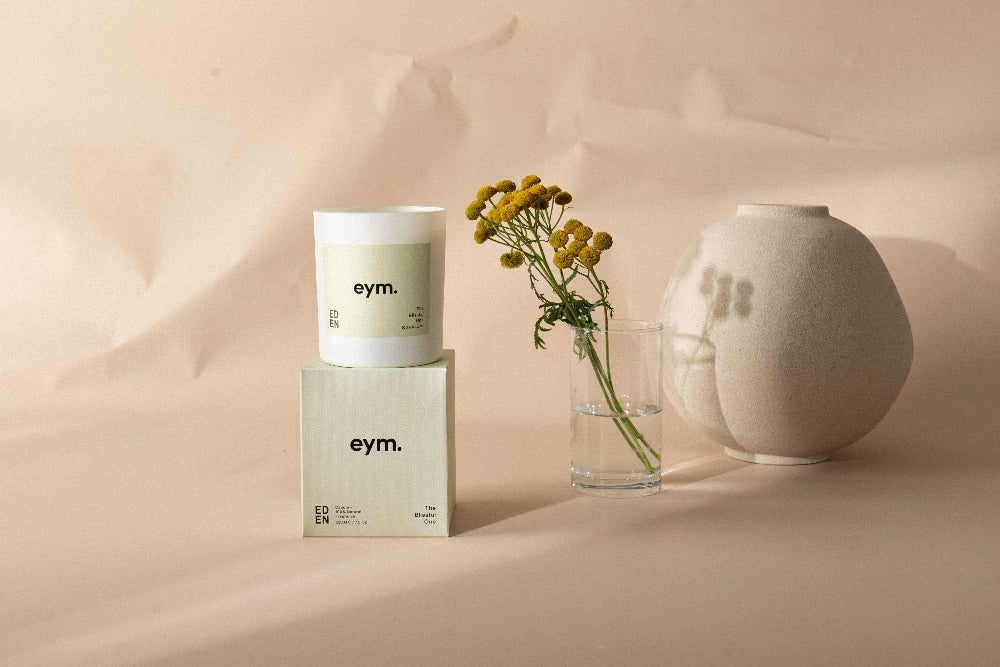 eym. products including a candle jar, box, and vase on a beige background