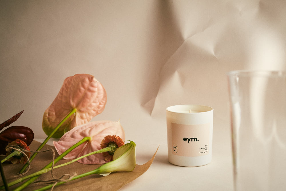 Candle with 'eym.' branding on a surface with flowers.