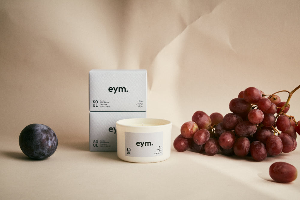eym candle with grapes and a plum on a beige background