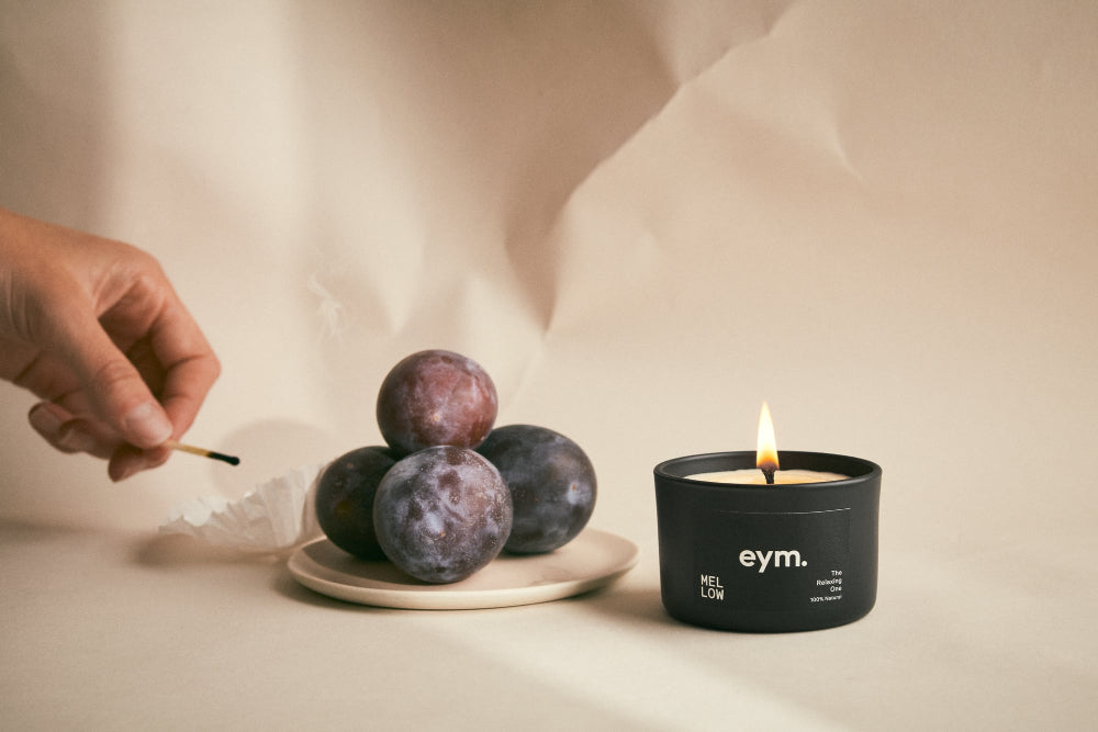 Candle being lit next to plums on a neutral background
