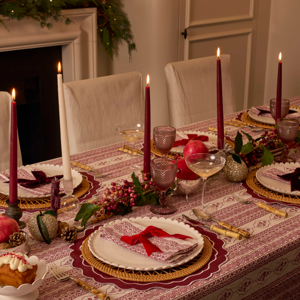 Decorated Christmas dining table with candles, glasses, and a cake in a festive setting.