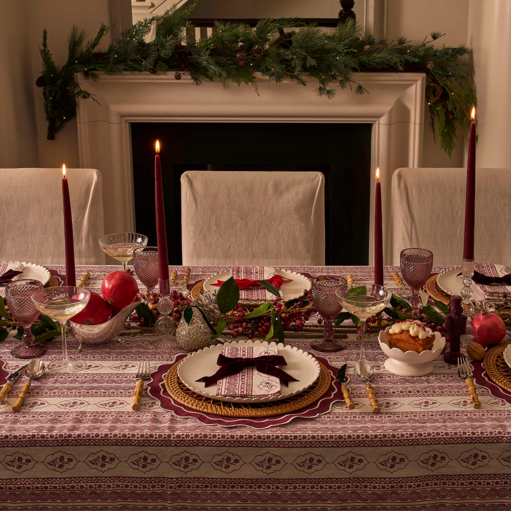 Dining table set for a festive meal with candles, place settings, and decorative items in front of a fireplace.