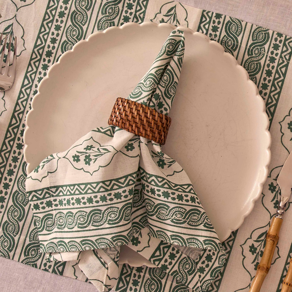Patterned napkin with a wooden napkin ring on a white plate against a decorative tablecloth.
