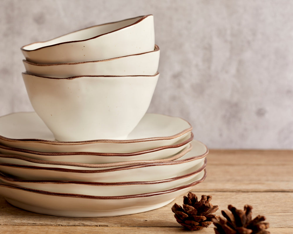 Stack of ceramic bowls with wavy edge design on a wooden surface.