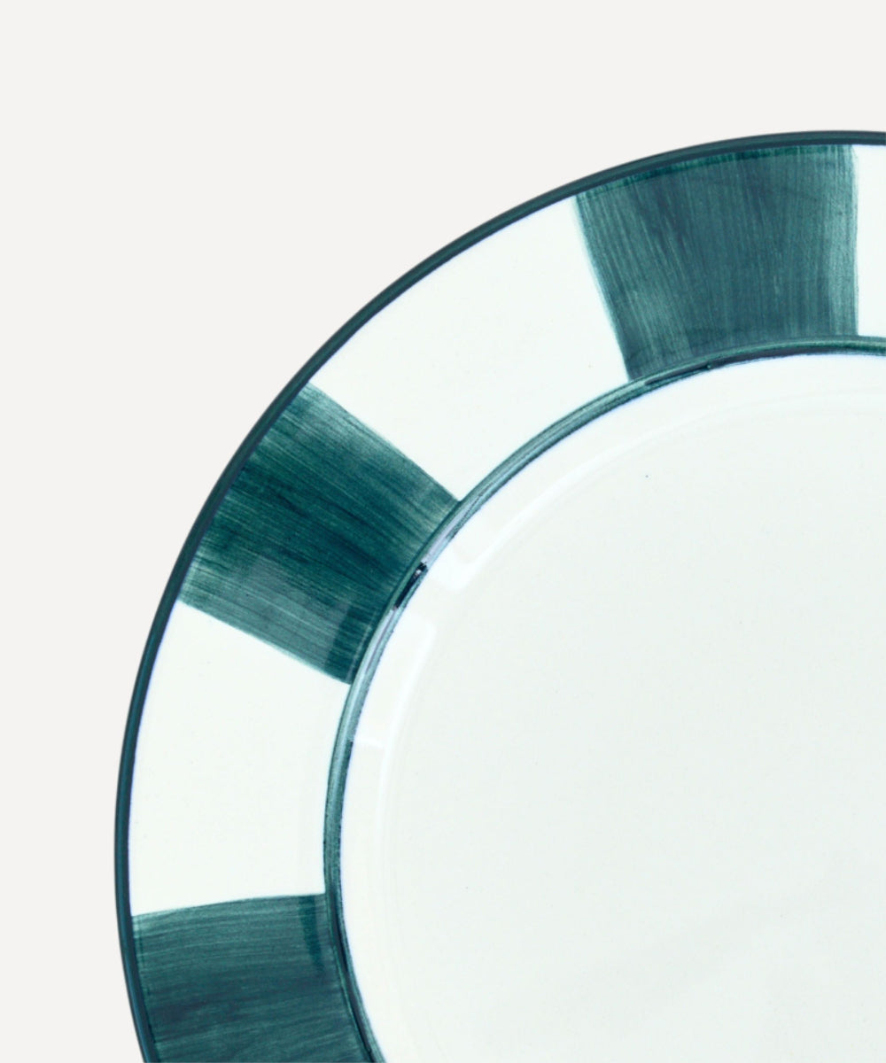 Closeup of Handmade ceramic dinner plate with teal painted stripes around edge on a white background.