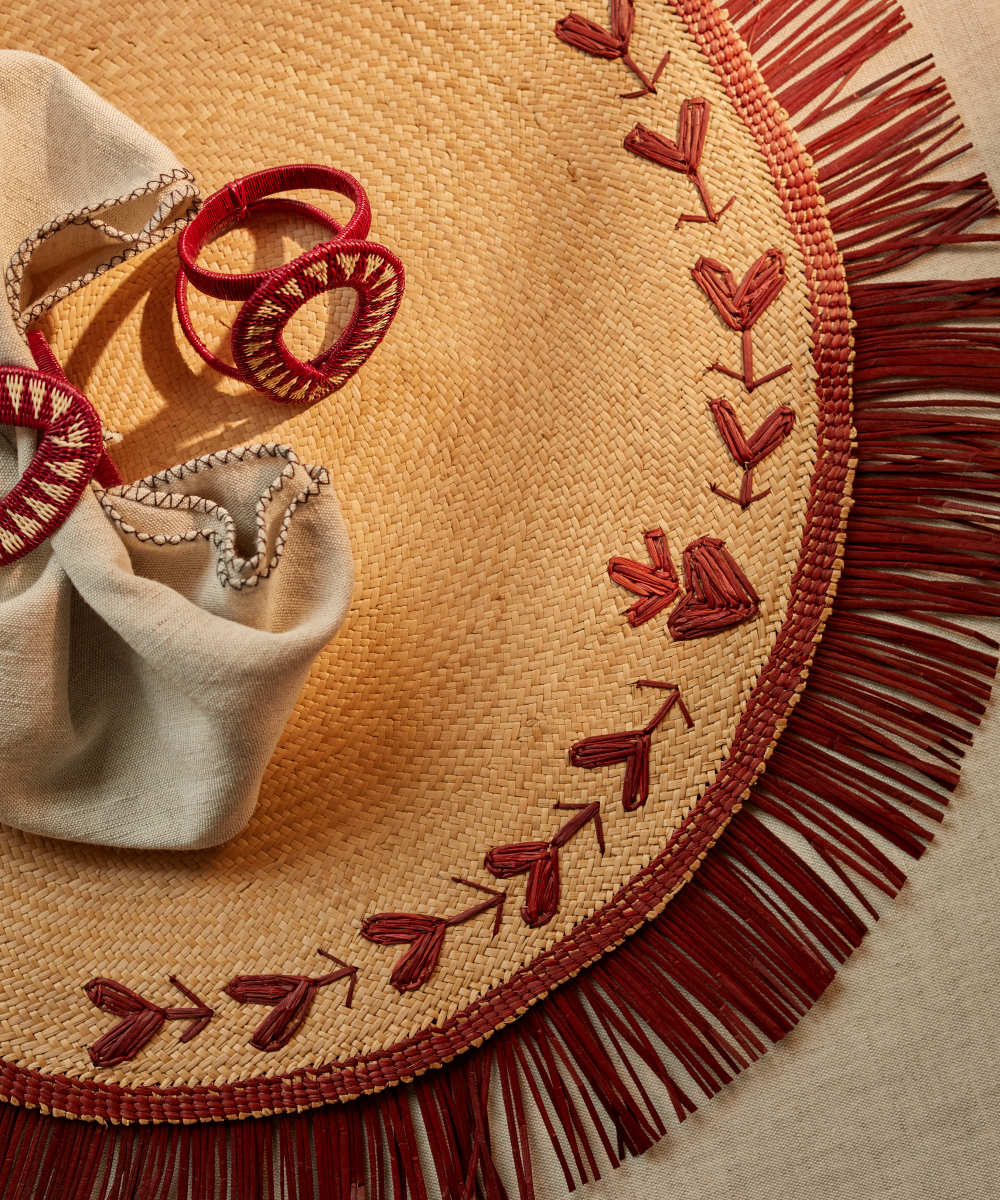 Woven mat with red embroidery and fringe, accompanied by a beige napkin and red napkin rings