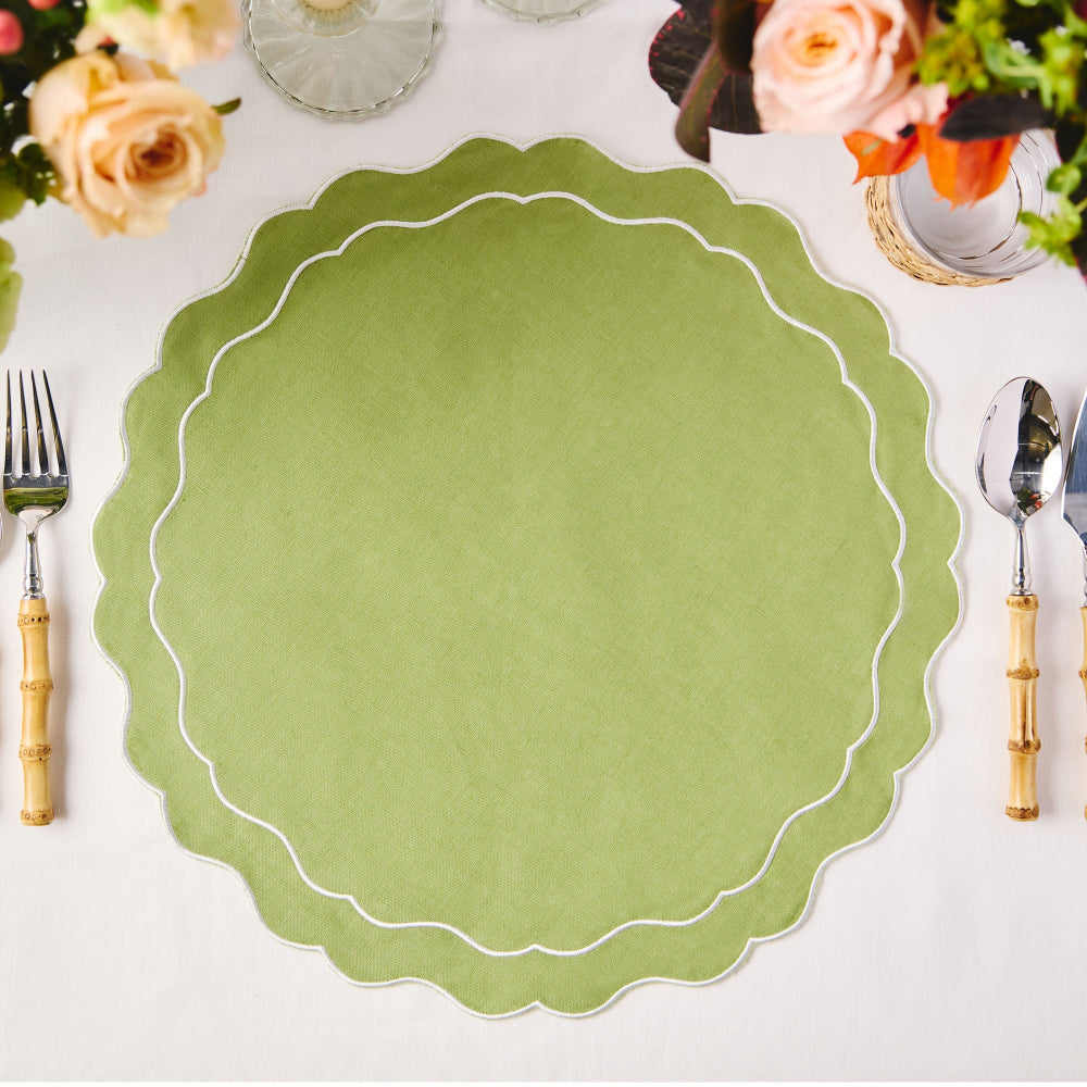 Green scalloped placemat on a white table with floral decorations and cutlery.