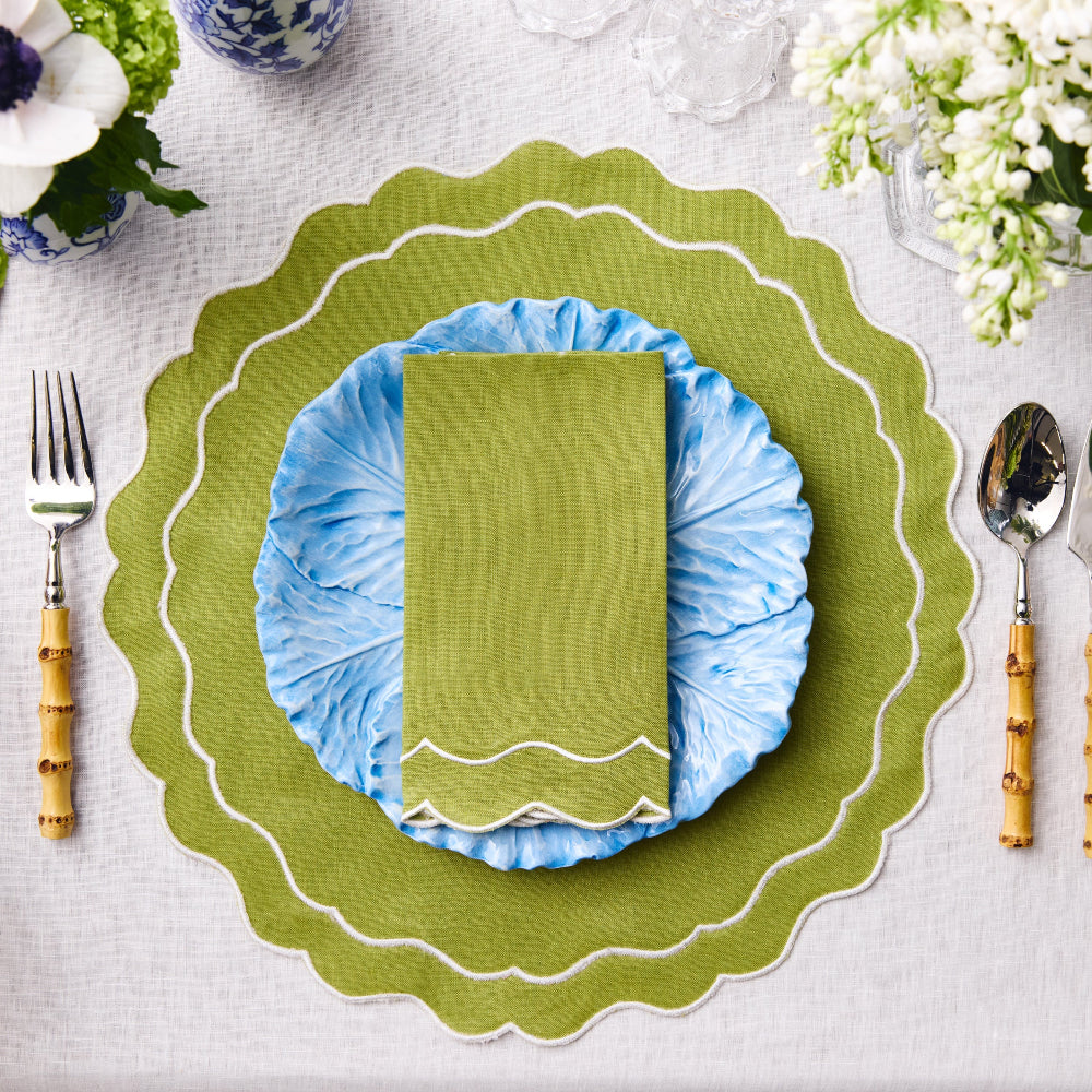 Table setting with green and blue plates, napkin, and cutlery on a white tablecloth.