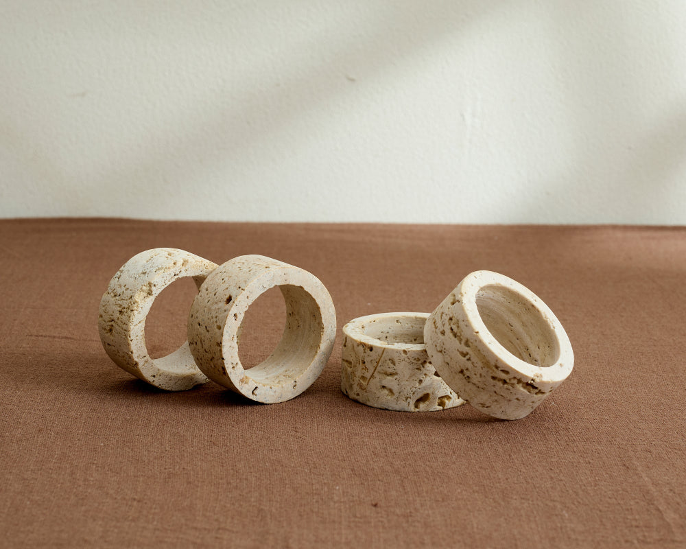 Set of four beige travertine napkin rings on a brown surface with a neutral background
