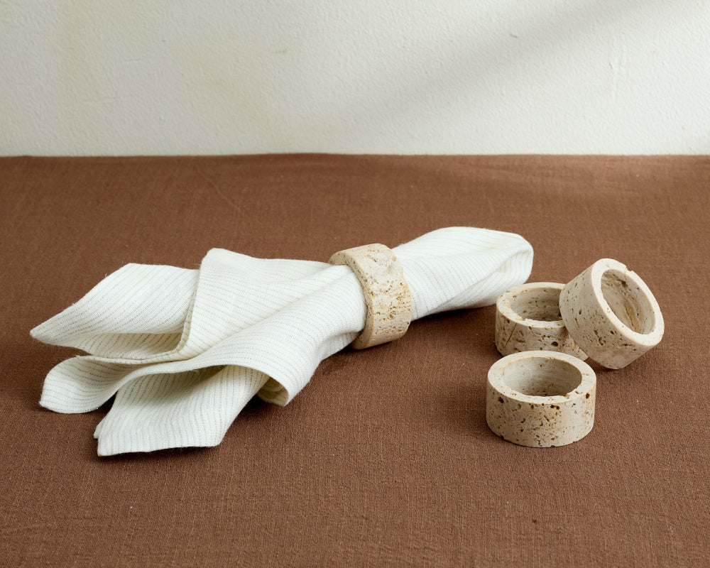Napkin with a travertine napkin ring and additional napkin rings on a brown surface