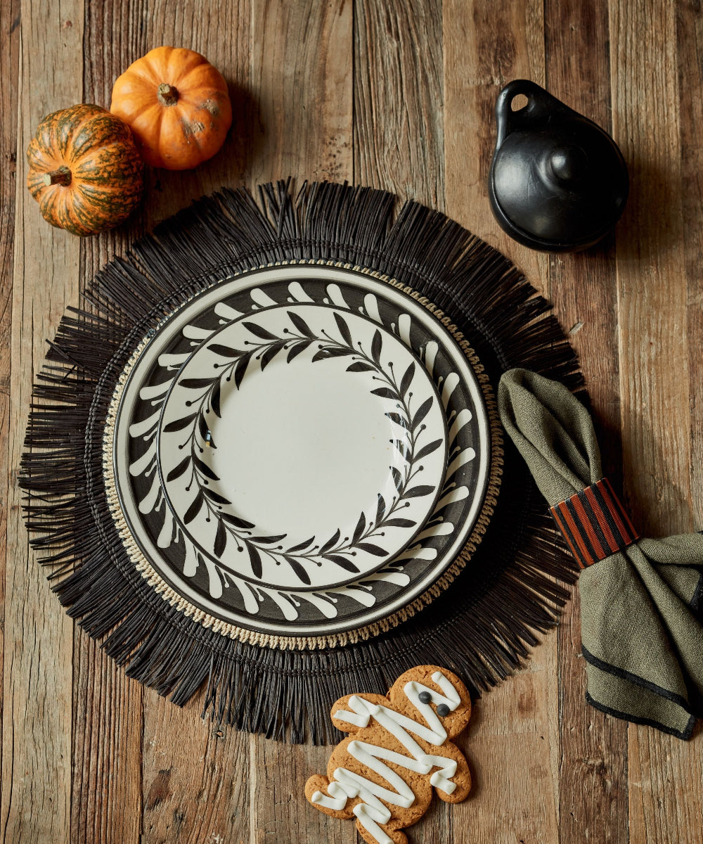 Lifestyle image of white ceramic plate with black handpainted fern leaves on a charger plate with pumpkins and gingerbread