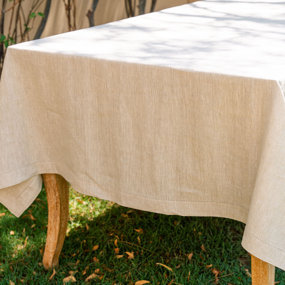 Natural beige tablecloth on a wooden table outdoors with grass and trees in the background