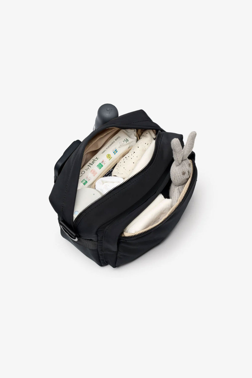 Black bag with baby items including a white blanket and grey toy on a light grey background