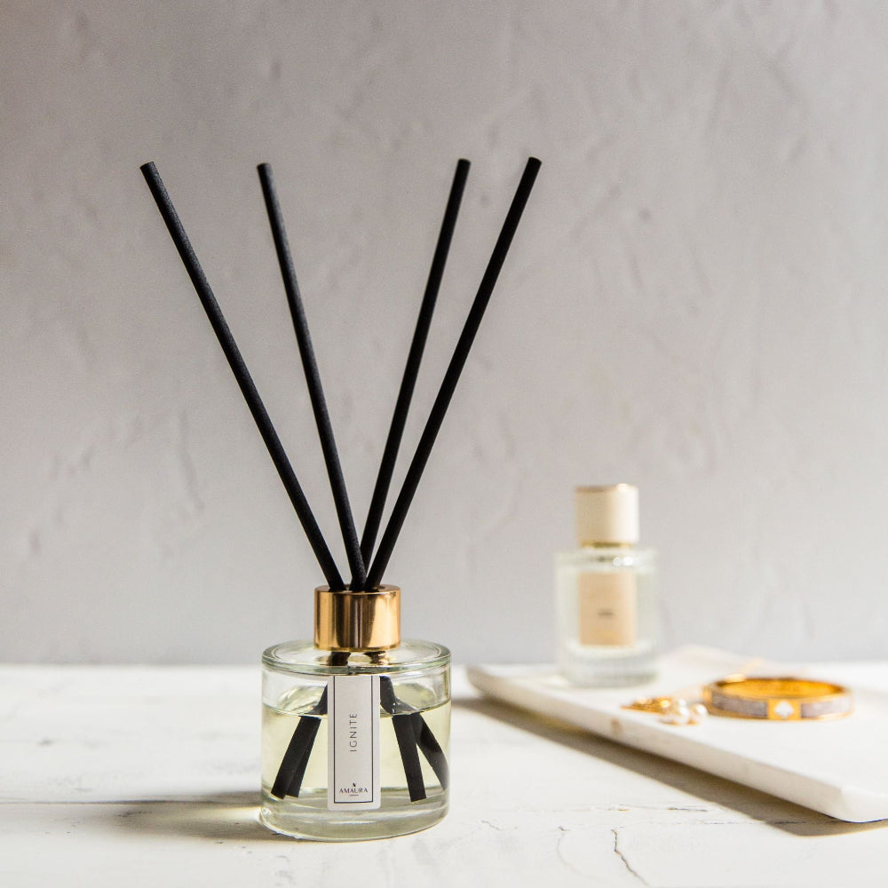 Reed diffuser with black sticks in a glass bottle on a light surface.