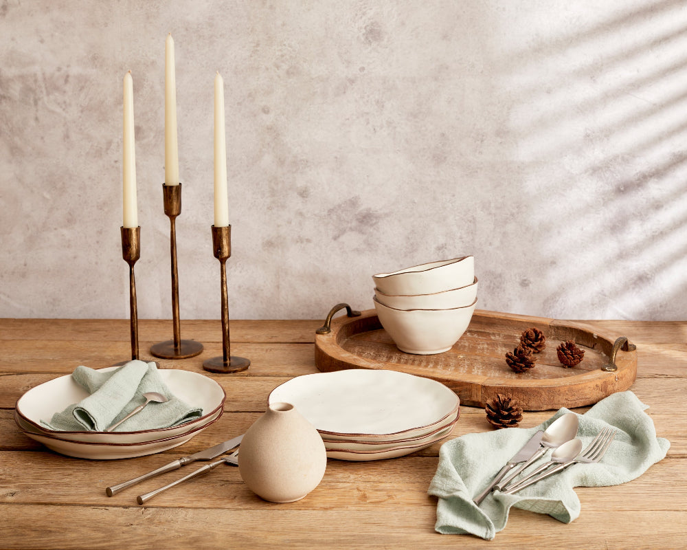 Dining table setting with ceramic plates, bowls, and cutlery on a wooden surface.