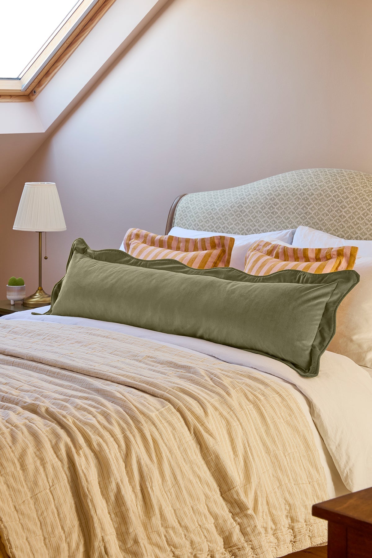 Bedroom with a bed featuring green and orange pillows, beige blanket, and a lamp.