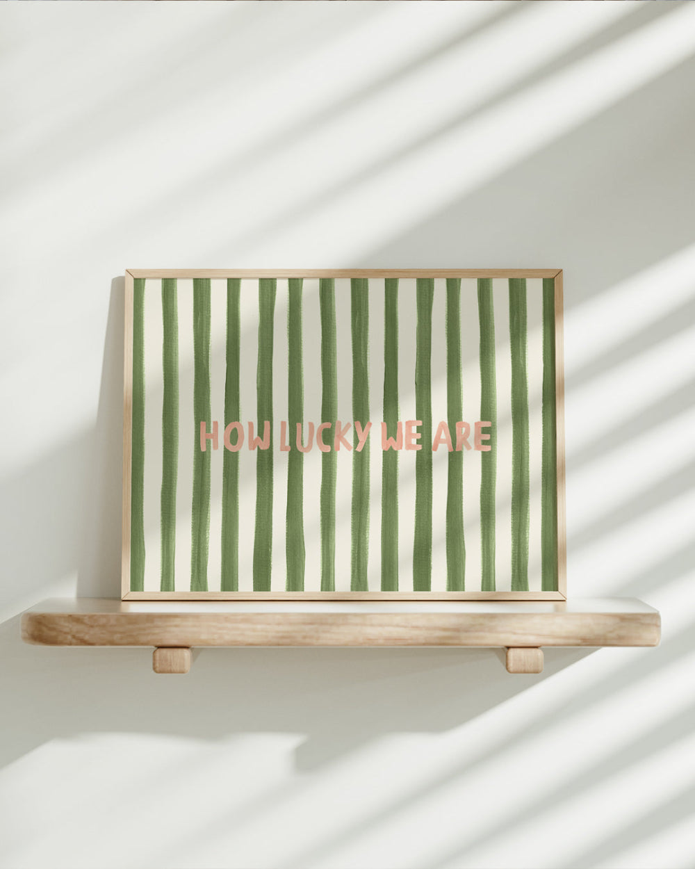 Framed artwork with green and white stripes and 'HOW LUCKY WE ARE' text on a wooden stand.