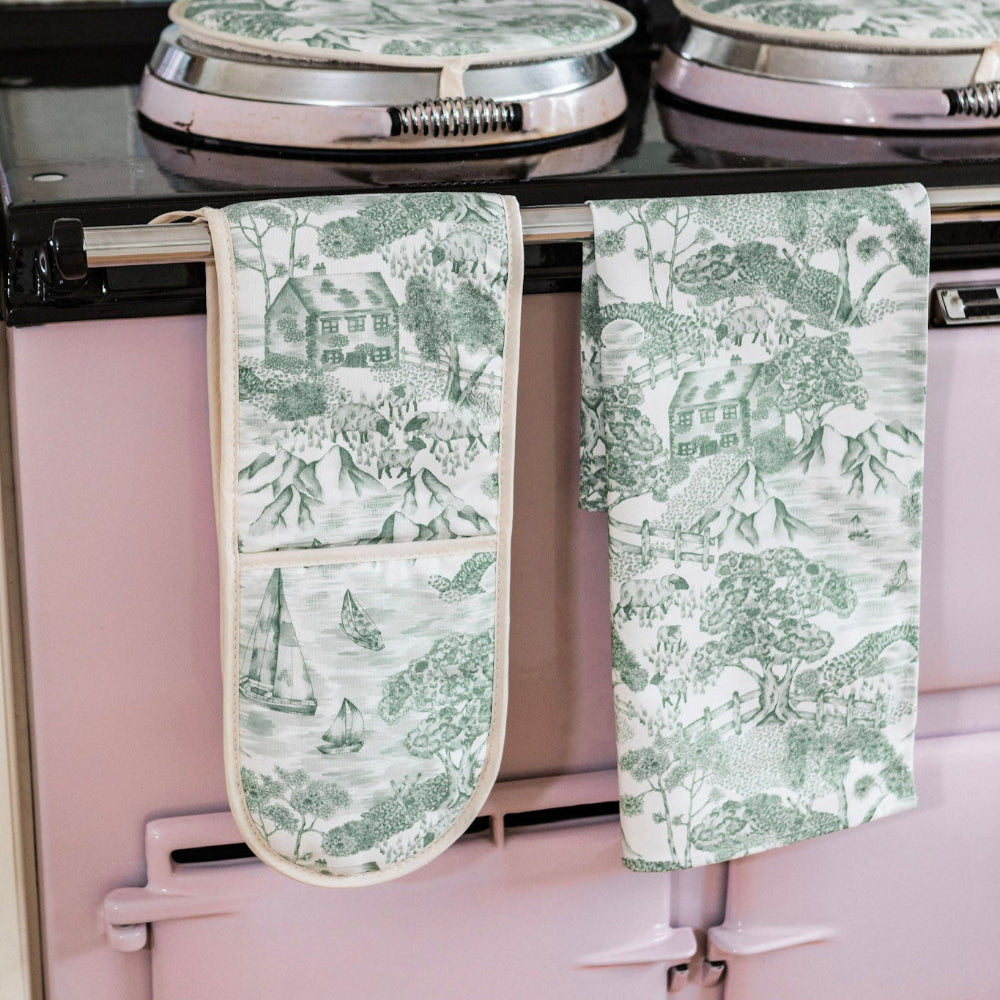 Green patterned oven mitt and towel hanging on a pink stove.