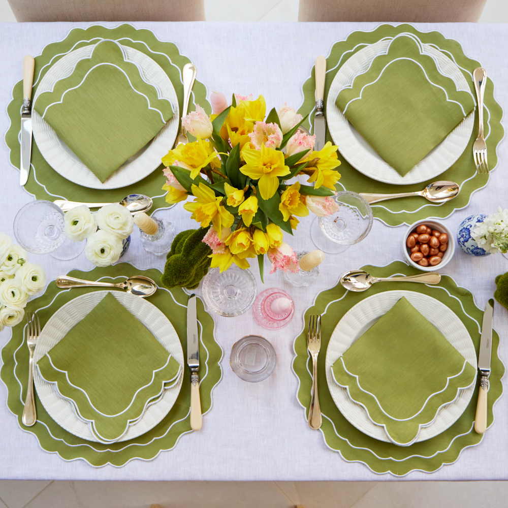 Elegant table setting with green placemats, white plates, and gold cutlery on a white tablecloth.
