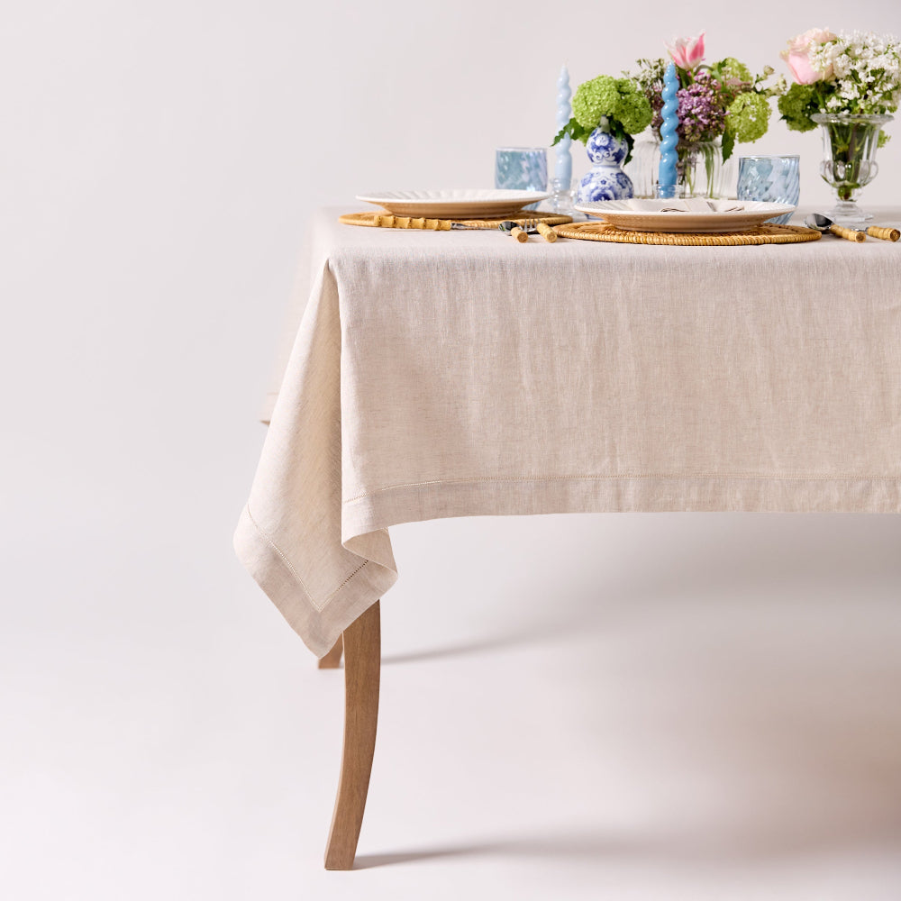 Table set with a beige tablecloth, plates, and floral arrangements on a white background
