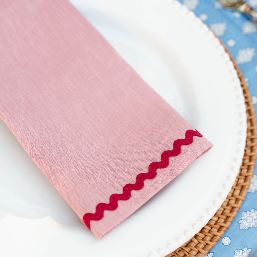 Pink Linen napkins with red wave trim on a white plate against a blue floral background