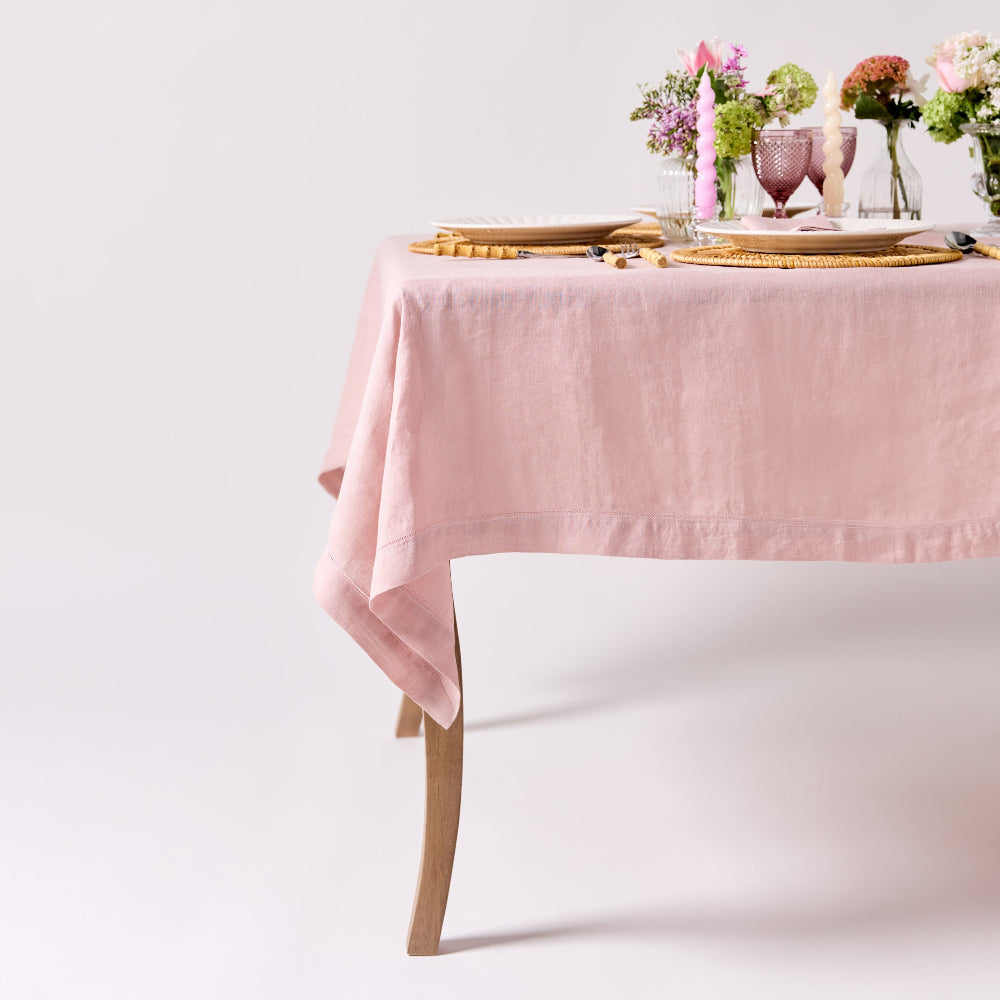 Table set with a pink tablecloth, flowers, and cutlery on a white background