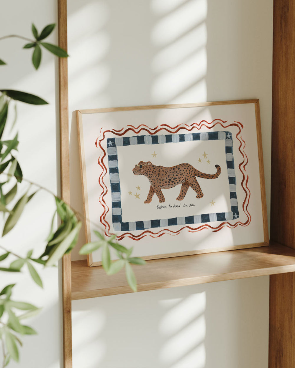 Framed artwork of a leopard on a white background with decorative border, placed on a wooden shelf.