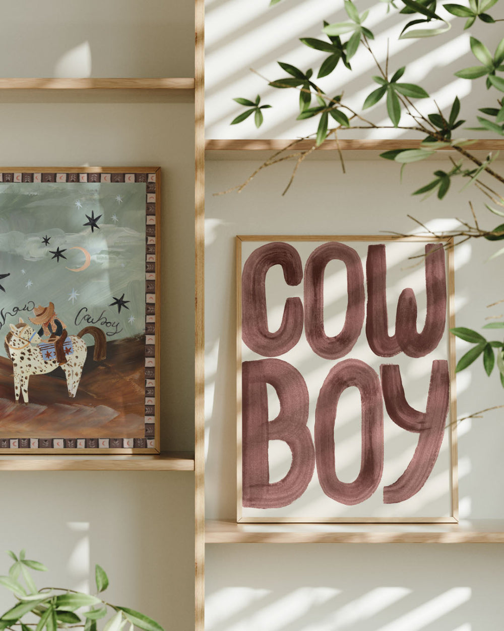 Framed artwork with 'CowBoy' text and another illustration on a wall with plants.