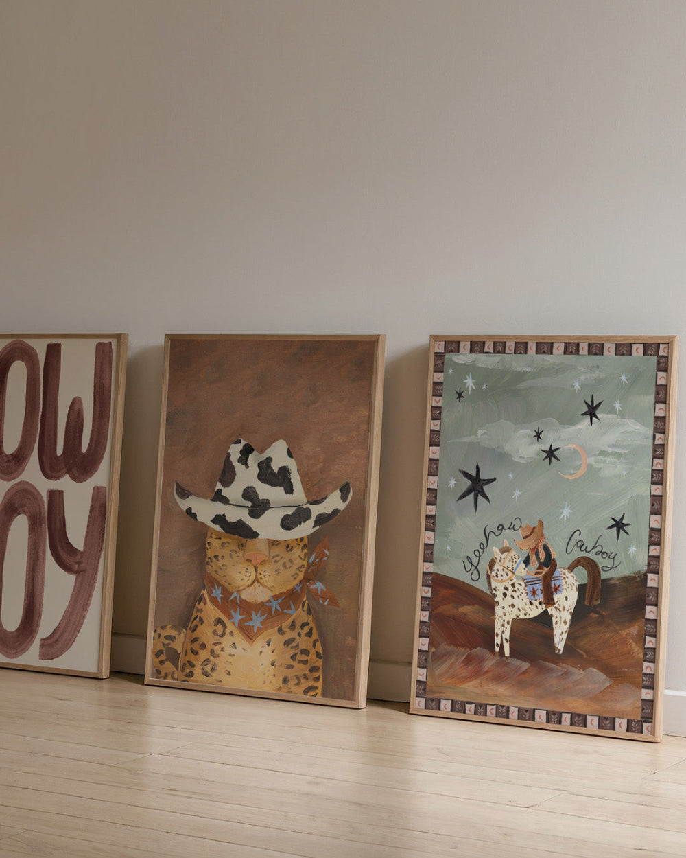 Three framed artworks on a wooden floor against a plain wall.